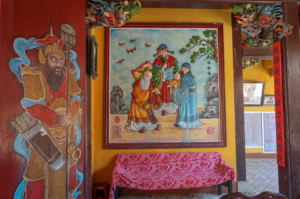 Wall paintings and guardian mural at Trieu Chau Assembly Hall Hoi An – Vibrant artwork depicting Chinese deities and mythological figures inside the temple.