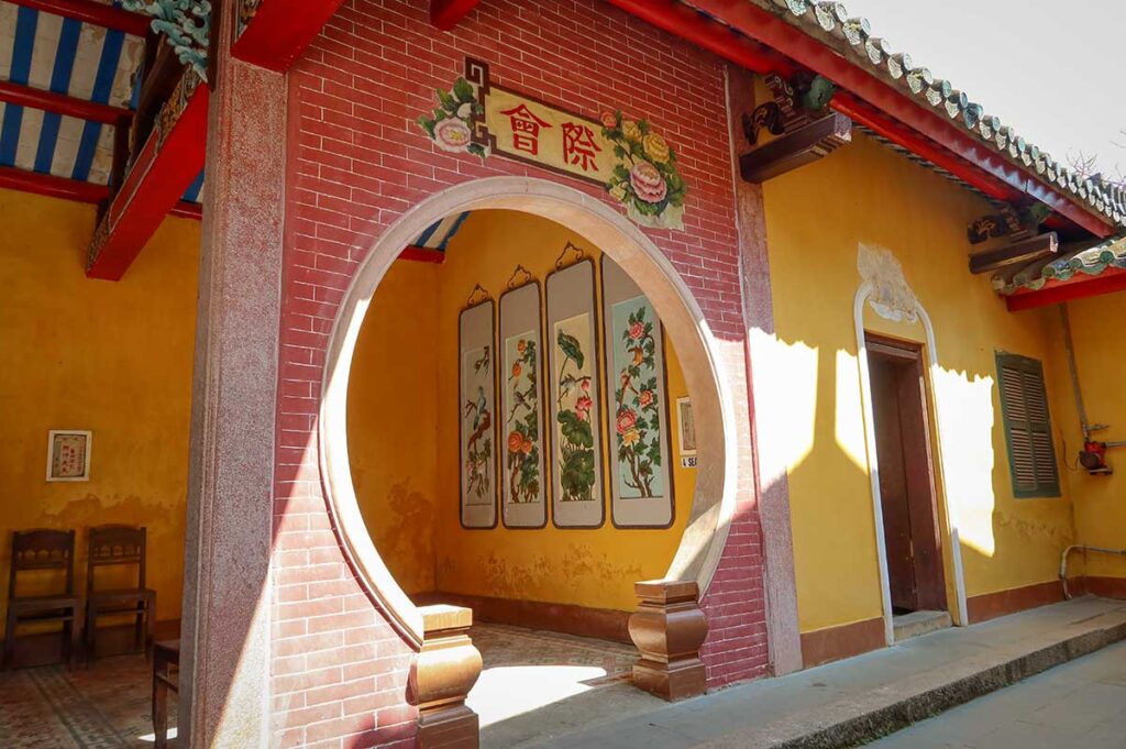 Circular moon gate inside Trieu Chau Assembly Hall Hoi An – Elegant round doorway framed by painted floral panels, leading into the temple’s inner courtyard.