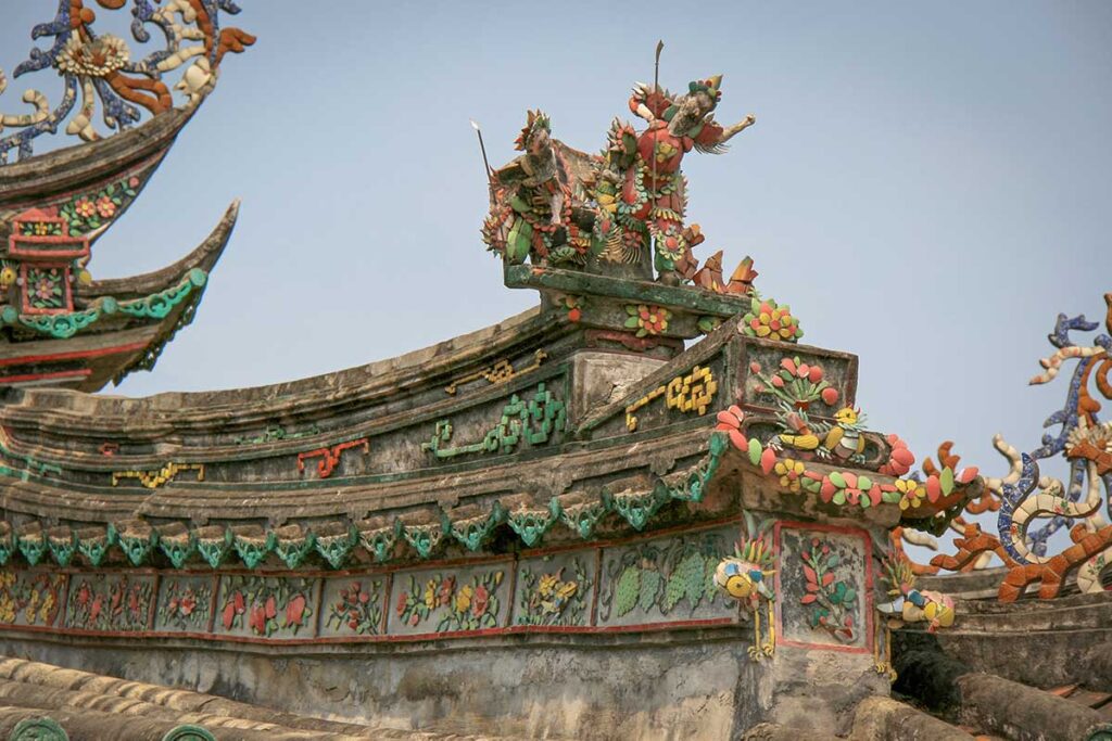 Ornate roof details at Trieu Chau Assembly Hall in Hoi An – Colorful ceramic dragon and warrior sculptures decorating the roofline of this historic Chinese assembly hall.