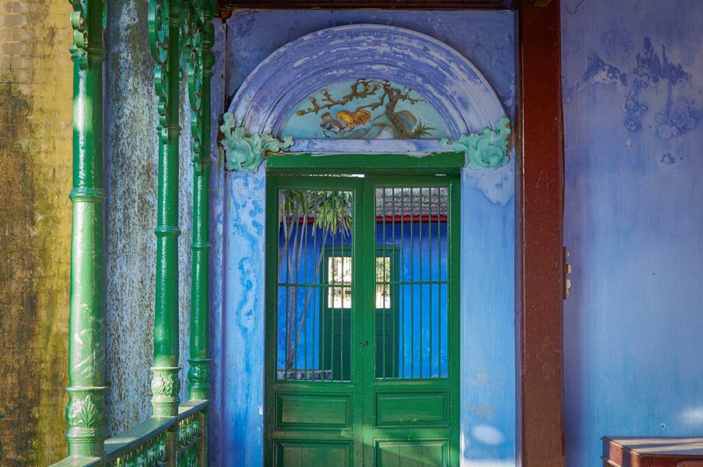 Colorful doorway inside Trung Hoa Assembly Hall in Hoi An, decorated with rooster painting and green wooden doors
