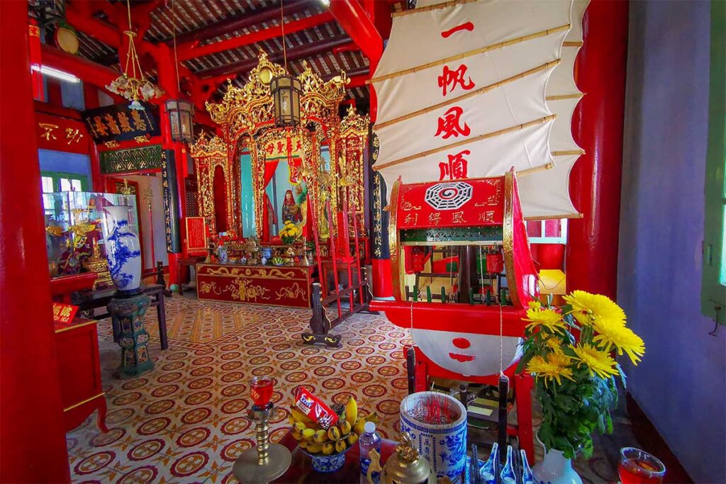 Trung Hoa Assembly Hall interior with gilded altar, bright red columns, and a symbolic model junk used in prayers for safe voyages.