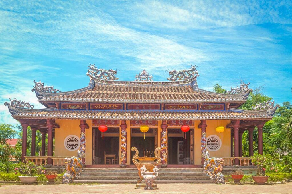 Front view of Van Thanh Khong Mieu Temple in Tam Ky, Quang Nam, with ornate roof details, red lanterns, and dragon pillars.