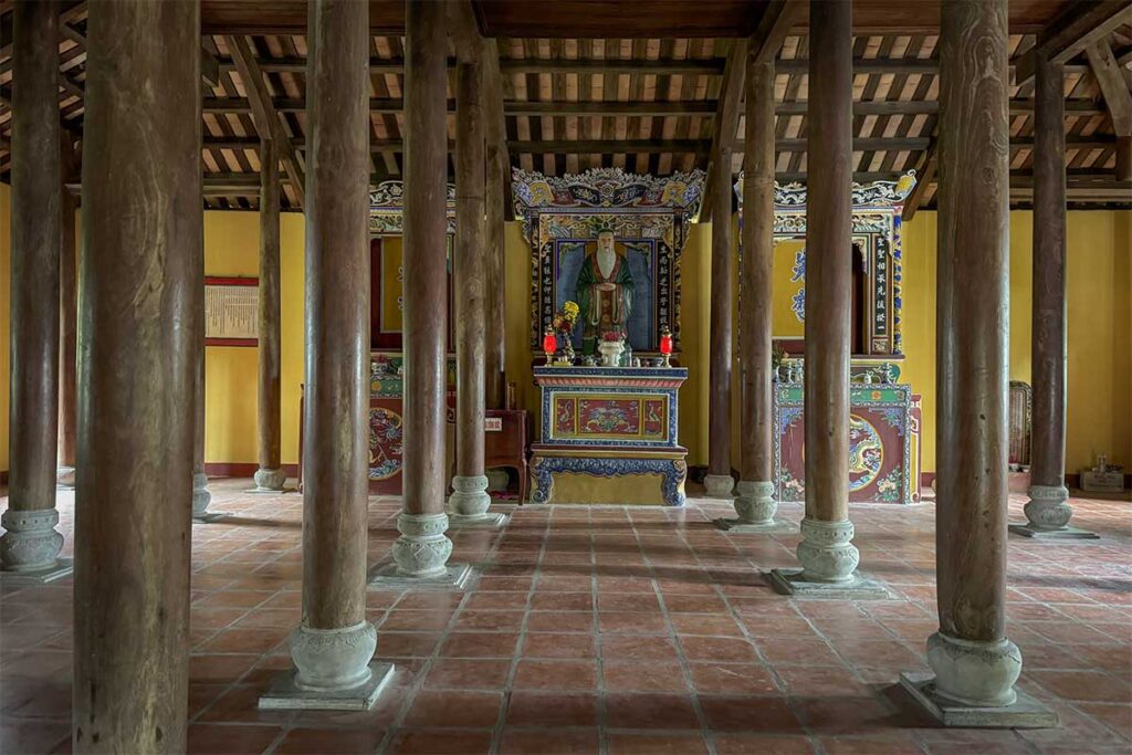 Interior of Van Thanh Khong Mieu Temple in Tam Ky, Quang Nam, showing wooden columns and a Confucian altar with incense.