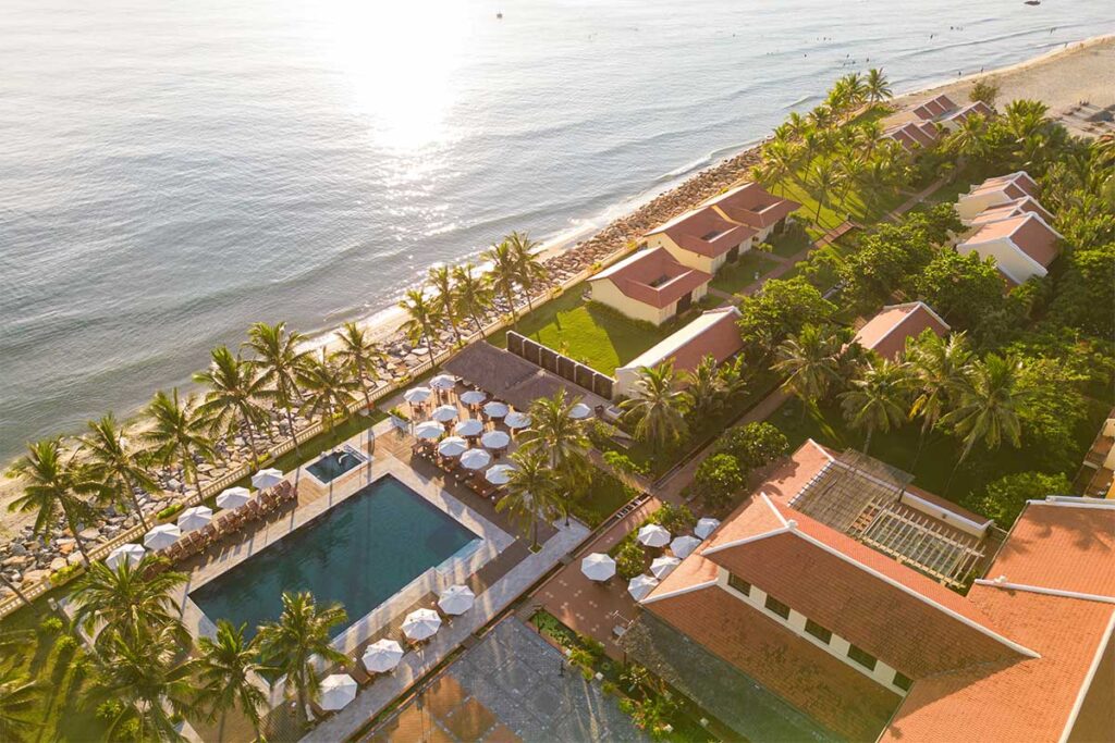 Aerial view of Victoria Hoi An Beach Resort at Cua Dai Beach, featuring a beachfront pool, palm trees, and traditional-style villas.
