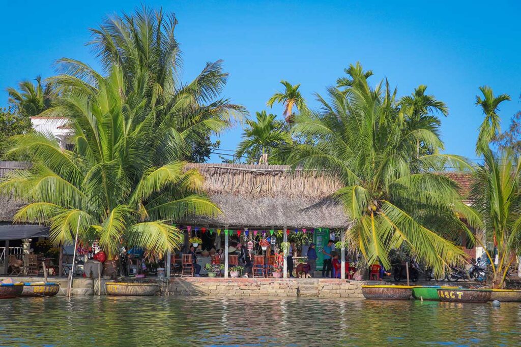 Traditional riverside houses and basket boats shaded by coconut palms in Cam Thanh Village, part of the Hoi An countryside