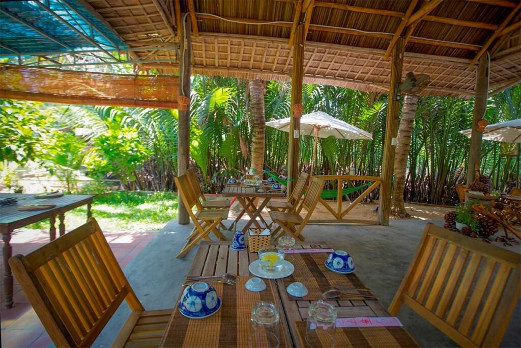 Bamboo and thatched roof restaurant in Cam Thanh Coconut Village surrounded by lush coconut palms.
