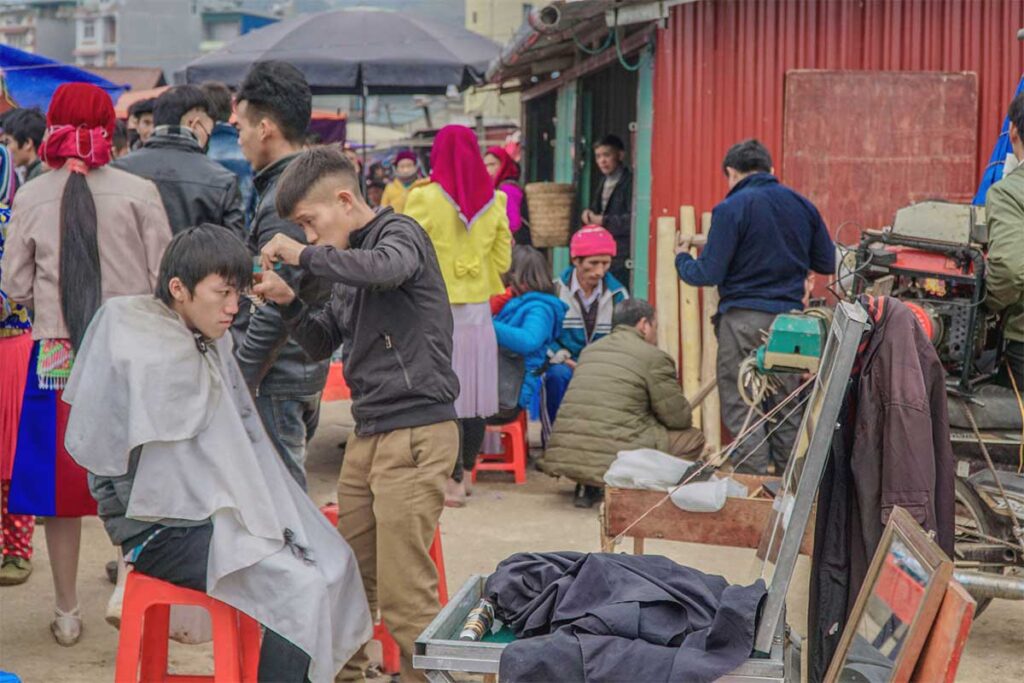 A barber cutting hair of a man outside right on the market streets of Dong Van