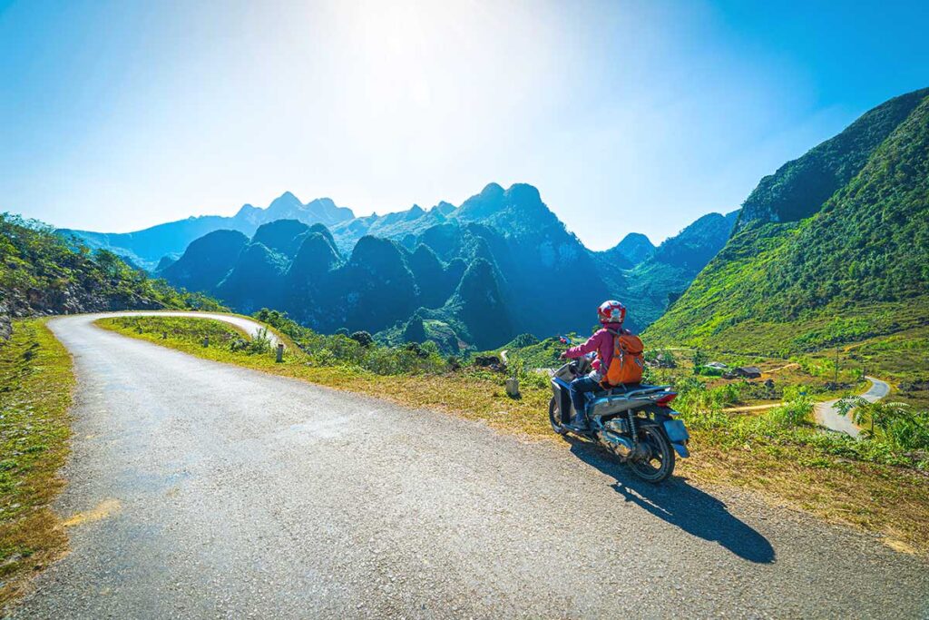 A tourist stopping on her motorbike along the road of the Ha Giang Loop with mountain views