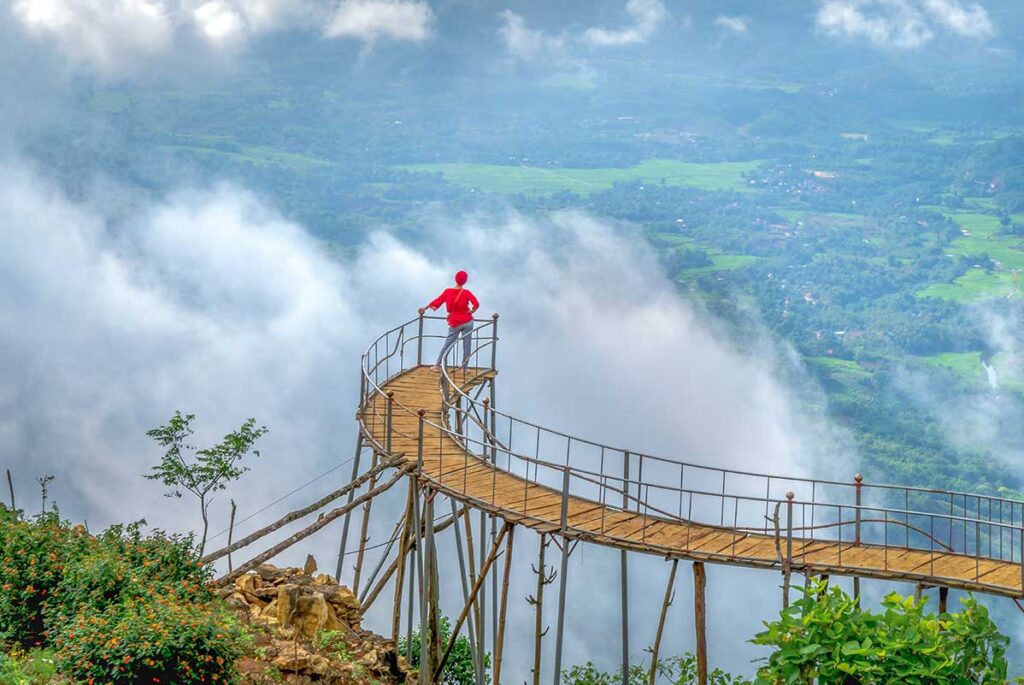 A woman in red standing a platform looking over the clouds in the valley below her at Hang Kia Cloud Hunting Viewpoint