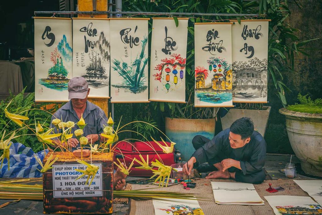 Local artists in Hoi An creating traditional calligraphy and handmade paintings sold along the street — authentic cultural souvenirs to take home