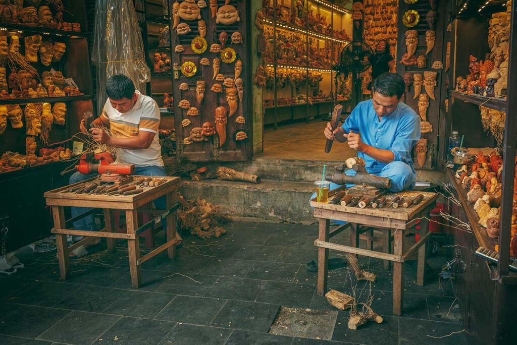 Artisans carving wooden masks and figurines at a souvenir shop in Hoi An — unique hand-carved gifts reflecting Vietnamese craftsmanship