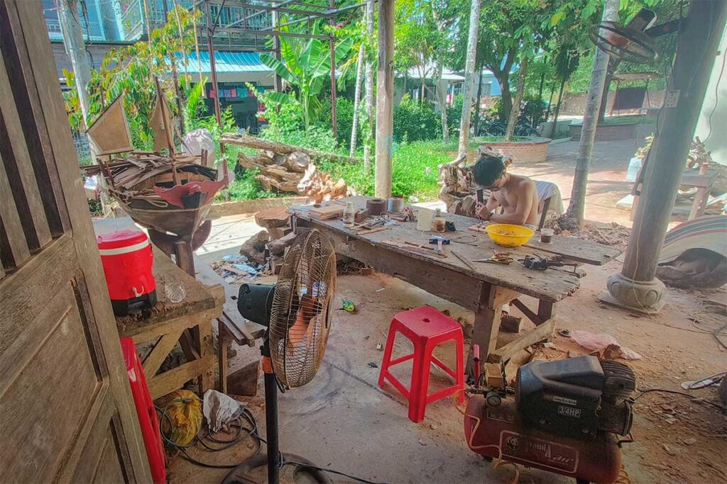 Woodworkers crafting wooden models and furniture at Kim Bong Village, a famous Hoi An craft village with centuries of carpentry heritage.