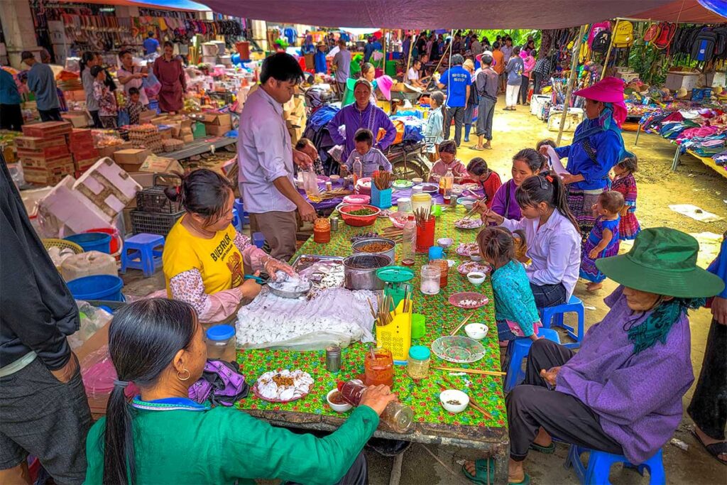 Local ethnic people sitting around a table enjoying food and having a chat at the Lung Khau Nhin Market
