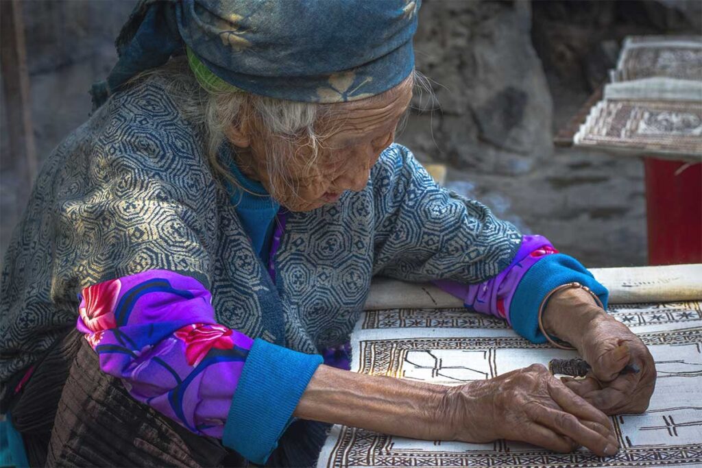 An elderly ethnic woman making designs on fabrics at Lung Tam Village