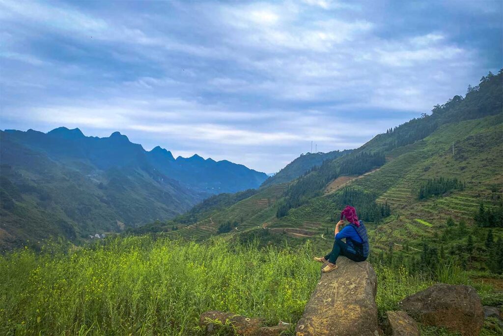 Ethnic minority woman sitting on a rock overlooking a valley with mountains and rice fields in Meo Vac District, Ha Giang