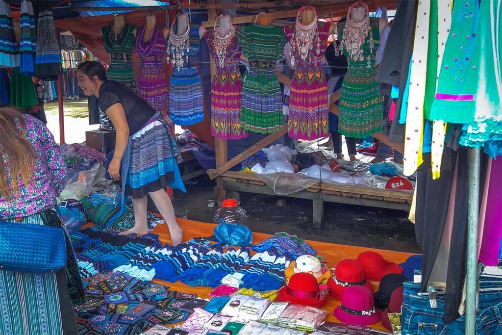 A colorful and traditional dressed ethnic woman is selling clothes on a stall at the Muong Khuong Market