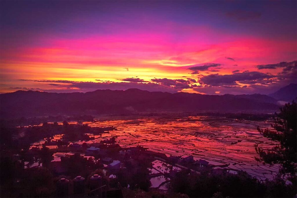 Rice fields of Muong Than seen from a viewpoint higher ip the hill during sunset with red sky that gets reflected by the water in the rice fields during watering season