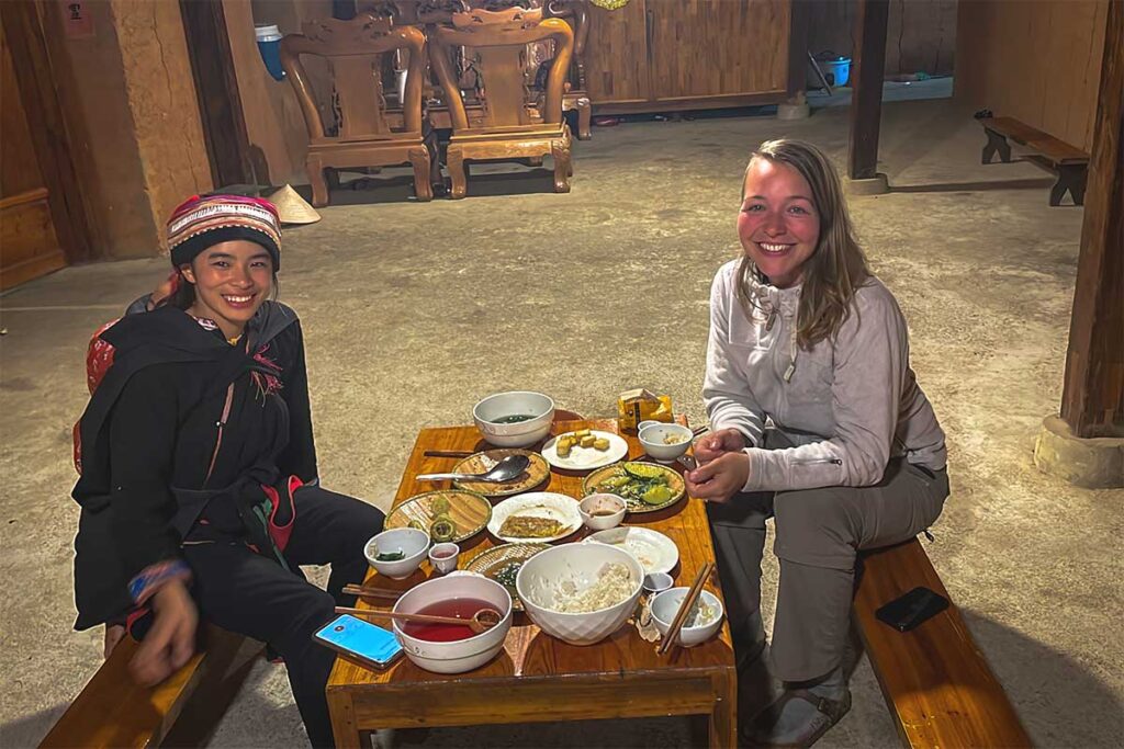 A foreign girl is having a family dinner with local ethnic Red Dao woman in a homestay in Nam Dam Village