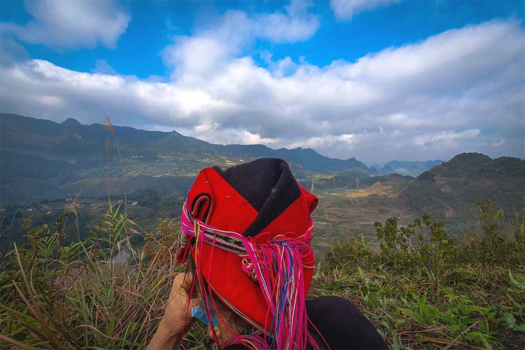 An ethnic Red Dao woman sitting on top of Nam Dam Hill with views over stunning mountain scenery