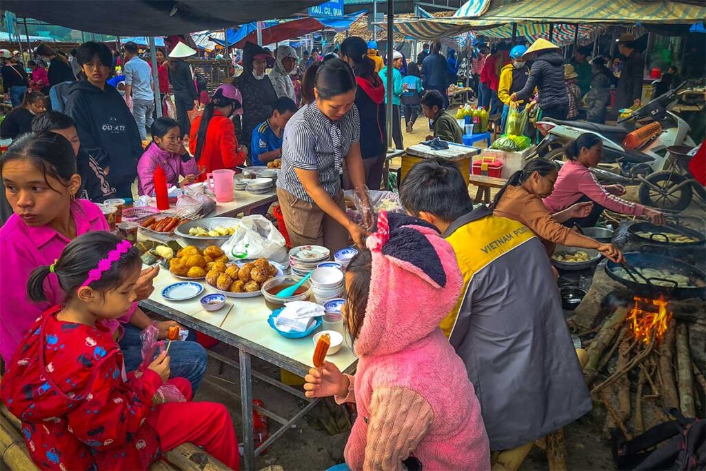 Busy street food scene with people buying snacks at a stall at the Pho Doan Market