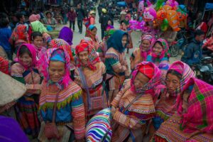 Ethnic minority women in vibrant traditional clothing at a lively hill tribe market in Sapa, Vietnam.