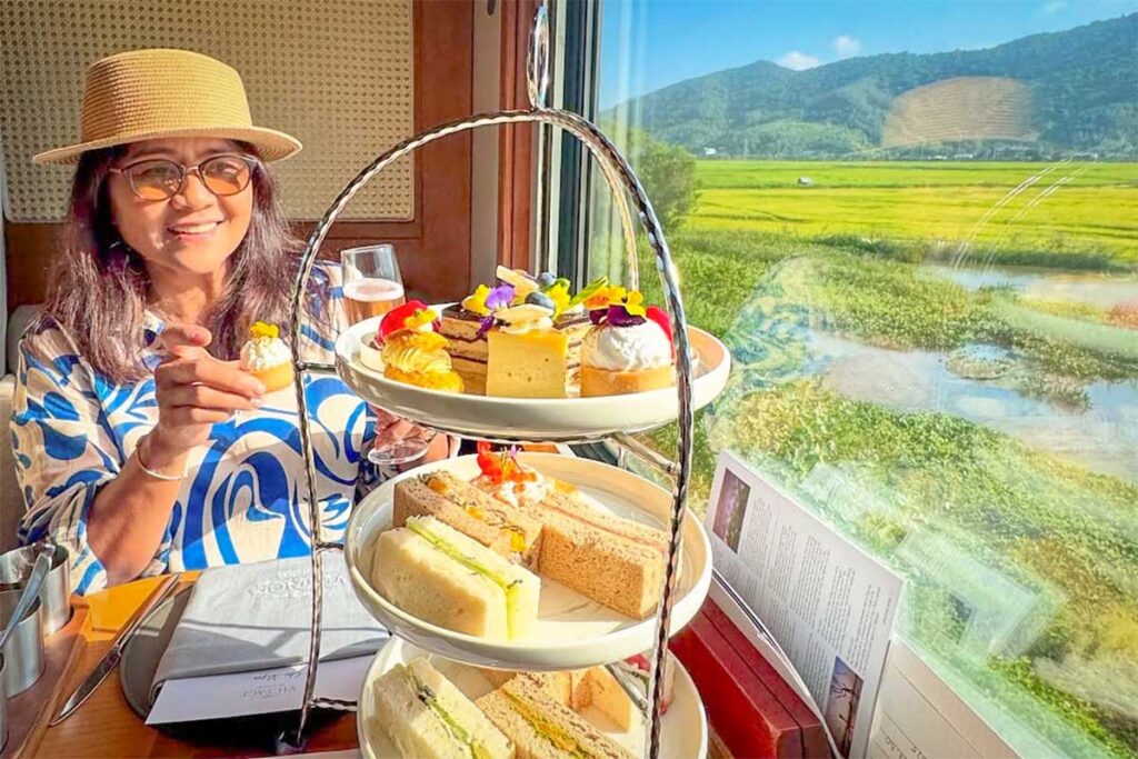 Passenger enjoying afternoon tea inside The Vietage luxury train while passing green countryside views in central Vietnam