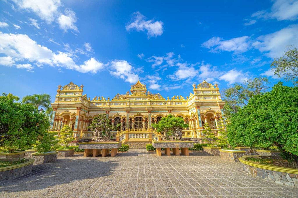 Main hall of Vinh Trang Pagoda in My Tho, Vietnam, showing the golden East–West influenced façade and landscaped gardens.