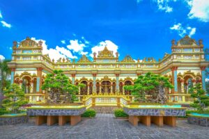 Front façade of Vinh Trang Pagoda’s main hall in My Tho, with ornate East–West architecture and bonsai trees displayed in the courtyard.