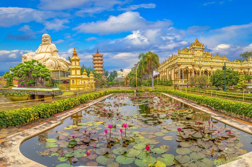 Panoramic view of Vinh Trang Pagoda with Maitreya Buddha, seven-story tower, main hall, and lotus pond filled with water lilies in My Tho, Tien Giang.