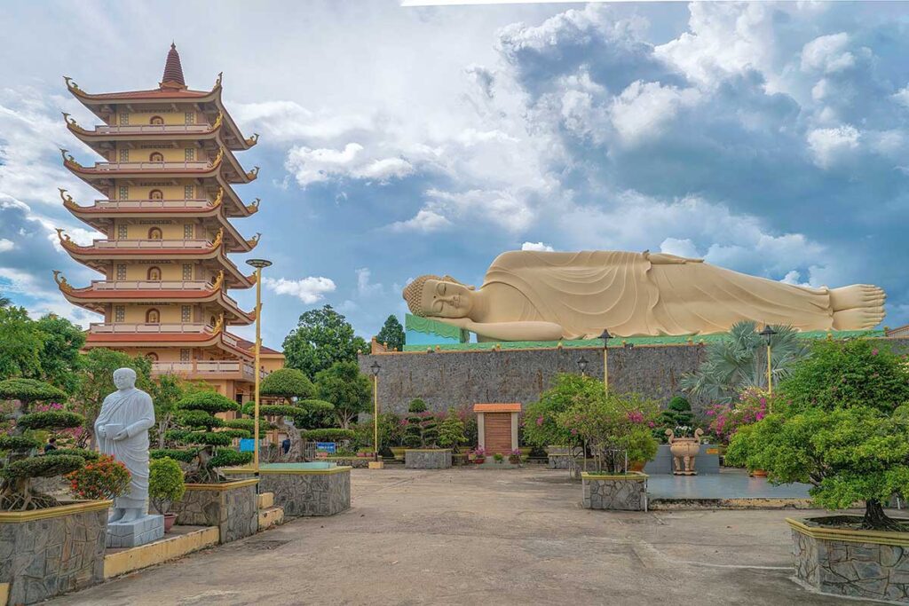 Seven-story tower and large reclining Buddha statue in the gardens of Vinh Trang Pagoda, a major Buddhist temple in the Mekong Delta.