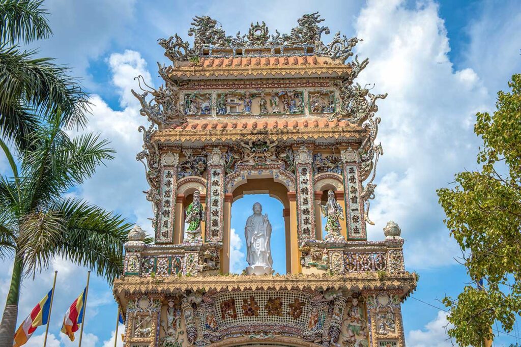 Ornate triple gate (Tam Quan) of Vinh Trang Pagoda in My Tho, decorated with ceramic mosaics, dragons, and Buddhist statues.