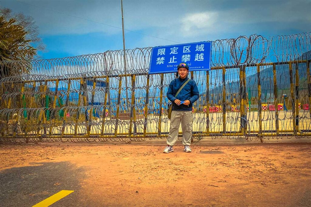A man standing in front of a wired gate on the border of Vietnam and China