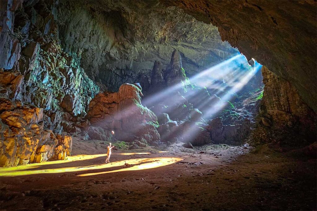 Amazing effect of light beams of the sun shining through the opening of Bat Cave on a traveller inside the cave