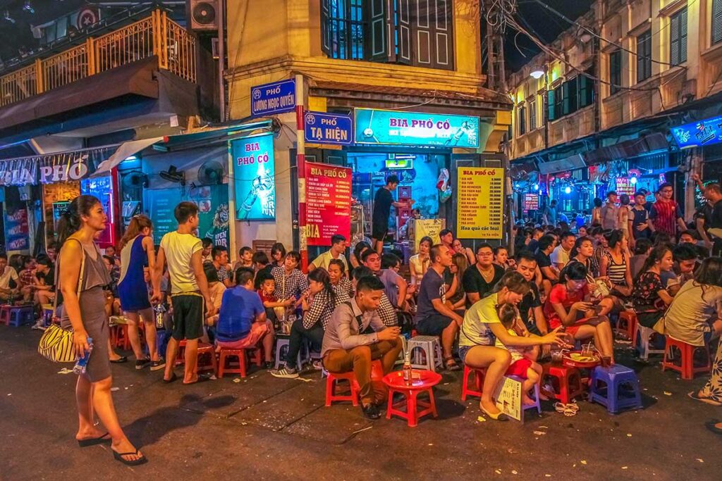 Bia Hoi Corner with low plastic chairs on the ground and drinking locals and tourists in Hanoi