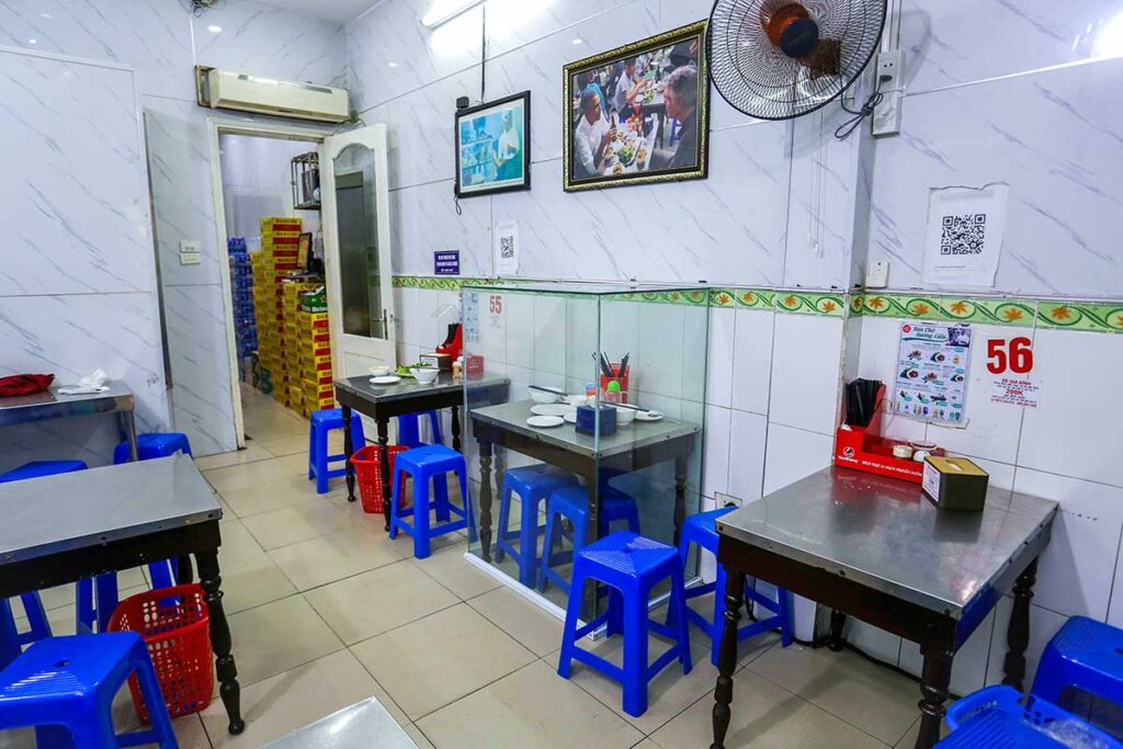 Bún Cha Huong Liên, inside the local Bun Chau Restaurant where a glass structure is set over a table and two plastic chairs where President Obama and Anthony Bourdain ate