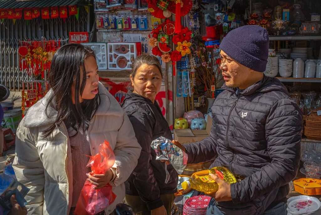A young Vietnamese woman buys cooking oil from regular vendors at Chau Long Market, Hanoi, Vietnam