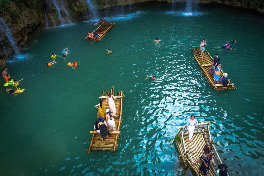 People swimming and using bamboo rafts at the Chieng Khoa Waterfall