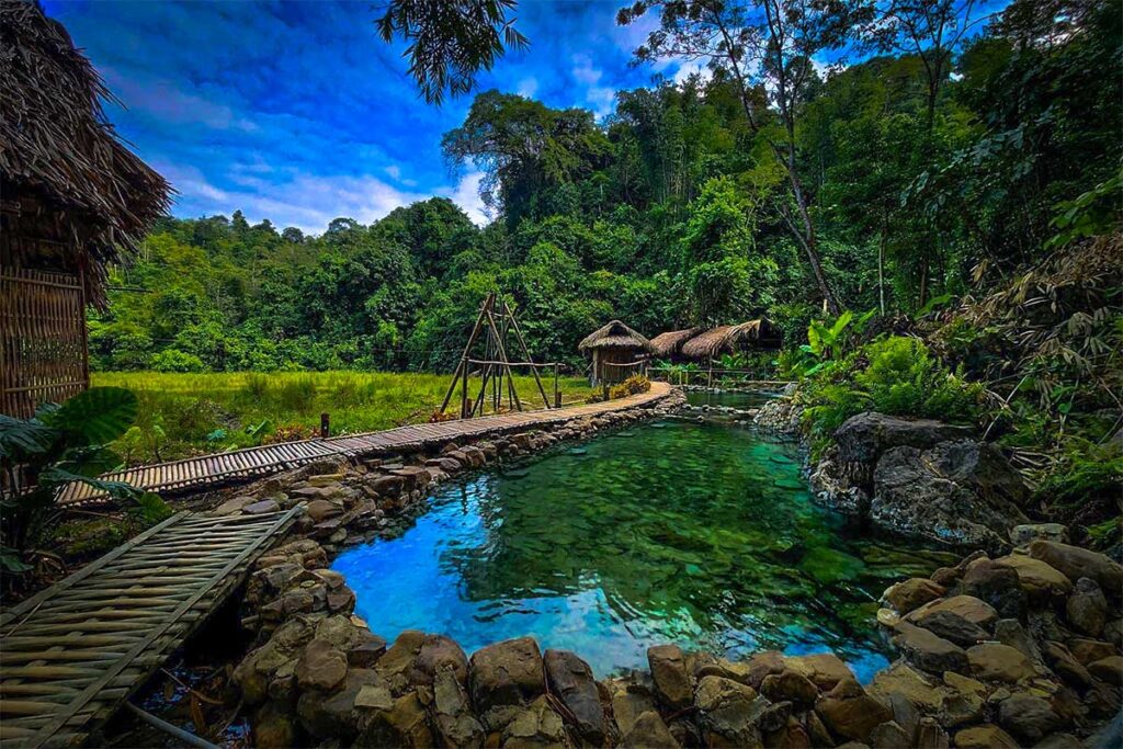A pool made out of natural stones with forest and rice fields in the background of Chieng Yen Hot Spring