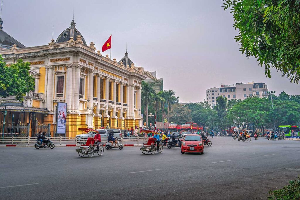 Hanoi Opera House in the background and, cars, motorbikes and cyclos driving through the streets of French Quarter Hanoi