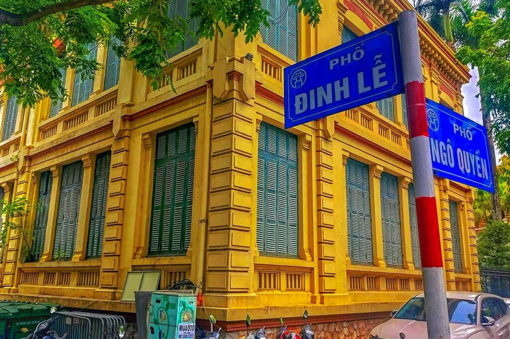 A street sign with yellow French Colonial building in the background in the French Quarter Hanoi