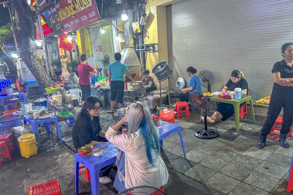 Locals eating street food on low plastic chairs at Hàng Buom Street in Hanoi Old Quarter