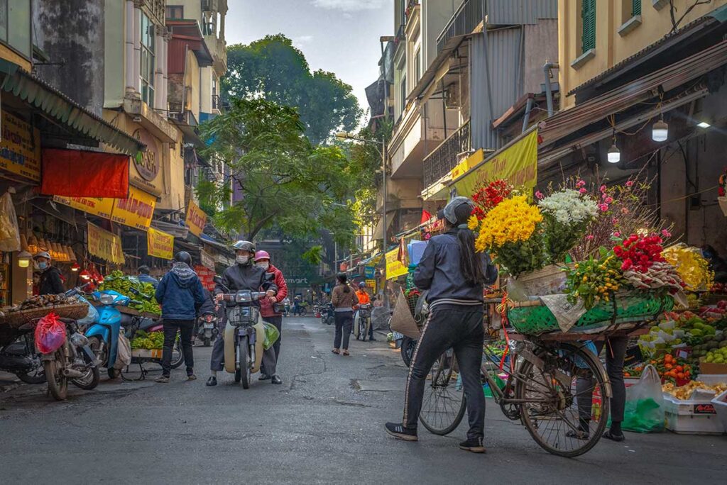 Hanoi Old Quarter in the early morning with quite street with some locals and a woman carrying flowers on her bicycle