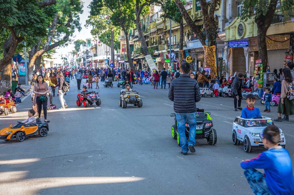Kids driving toy electric cars through the streets of the Old Quarter during Hanoi Weekend Night Market when there is no other traffic on the streets