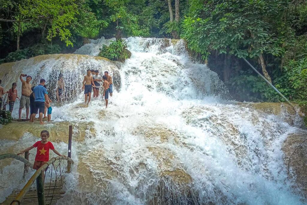 Vietnamese tourists standing in the Hieu Waterfall with a lot of water