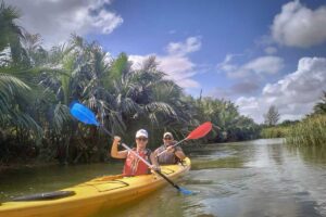 Two travelers kayaking through dense nipa palm mangroves under a bright sky during the Hoi An tour