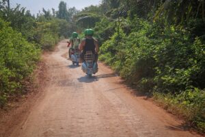Hoi An Vespa tour driving down a narrow red-dirt trail surrounded by tropical greenery