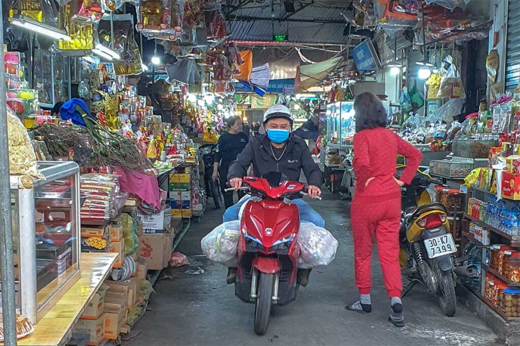 A motorbike with goods driving along the market stalls inside the Hom Market