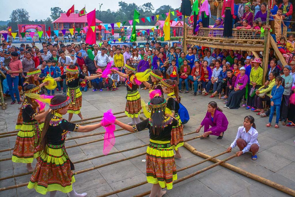 Kids in traditional clothes and adults are playing a game with bamboo sticks you have to jump over in a certain ritm during Hung Kings Festival