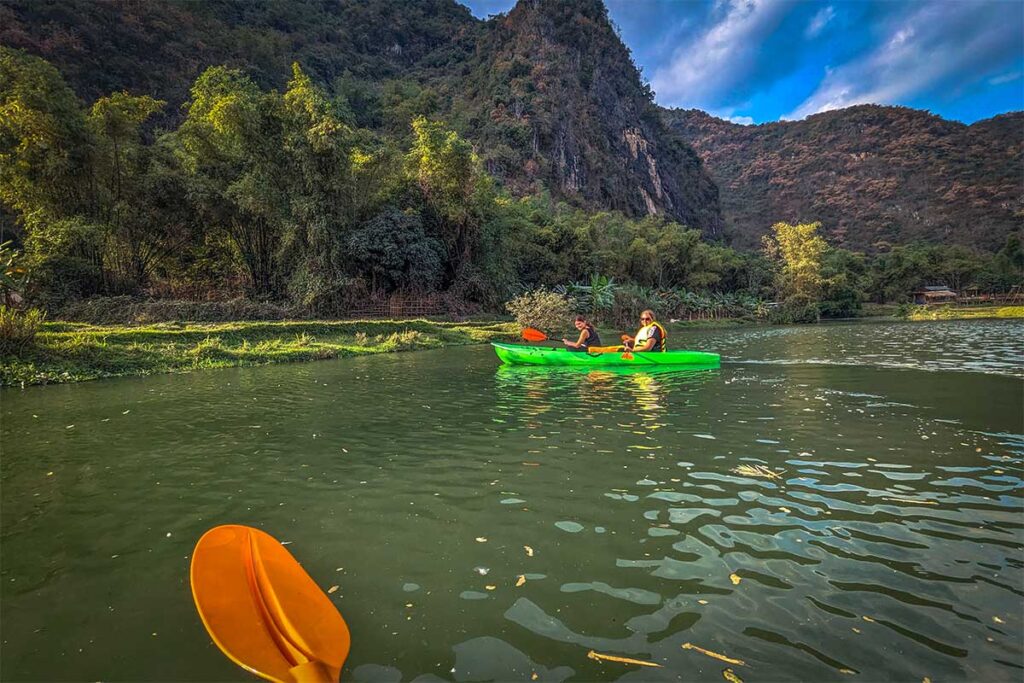 Two tourists in one kayak paddling over a local stream in Mai Chau