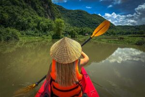 A foreign girl with conical hat is paddling in a kayak in Mai Chau over a local stream
